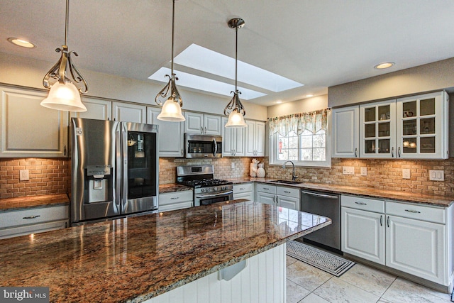 kitchen featuring dark stone countertops, a sink, decorative backsplash, stainless steel appliances, and glass insert cabinets