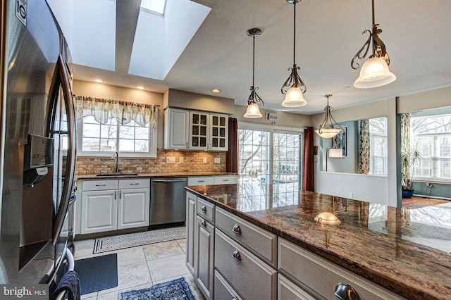 kitchen with backsplash, glass insert cabinets, a wealth of natural light, appliances with stainless steel finishes, and a sink