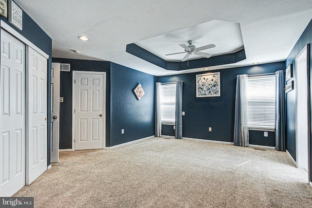 unfurnished bedroom featuring baseboards, a raised ceiling, carpet, and multiple windows