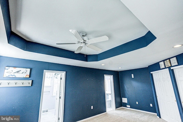 unfurnished bedroom featuring baseboards, visible vents, ensuite bath, a raised ceiling, and carpet flooring