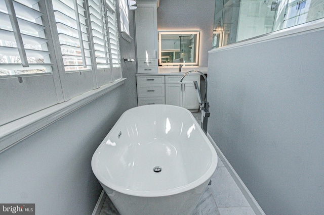 full bath featuring marble finish floor, vanity, baseboards, and a freestanding tub