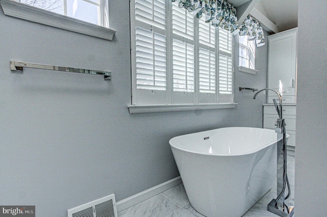 bathroom featuring visible vents, marble finish floor, a freestanding bath, and plenty of natural light