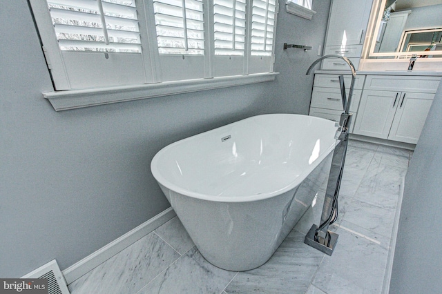 bathroom with visible vents, baseboards, a freestanding bath, marble finish floor, and vanity