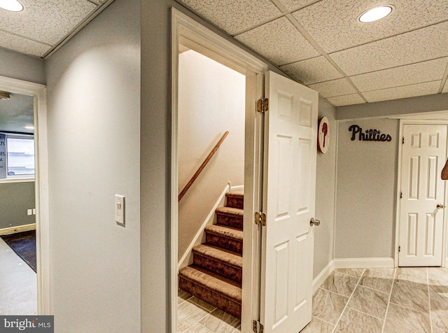 stairway featuring a paneled ceiling and baseboards