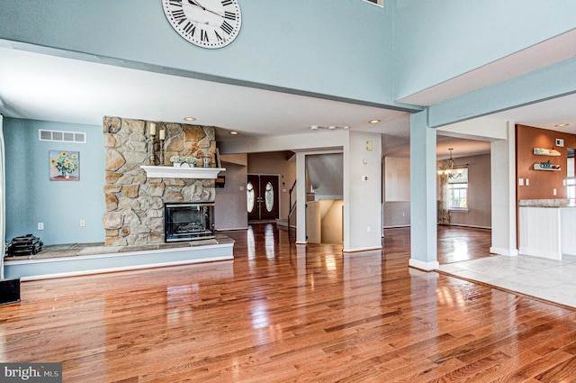 unfurnished living room with a stone fireplace, a notable chandelier, wood finished floors, and visible vents