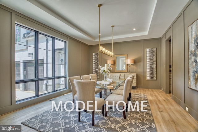 dining area with light wood-type flooring, a raised ceiling, and plenty of natural light