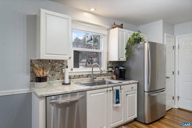 kitchen with appliances with stainless steel finishes, sink, light wood-type flooring, white cabinetry, and tasteful backsplash