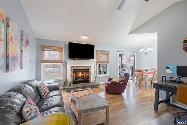 living room featuring a fireplace, ceiling fan with notable chandelier, light wood-type flooring, and vaulted ceiling