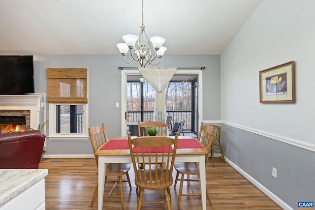 dining space featuring wood-type flooring, a stone fireplace, and a notable chandelier