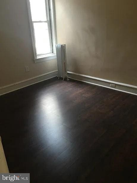 empty room featuring radiator and dark hardwood / wood-style flooring