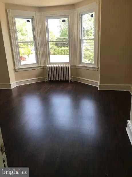 unfurnished room featuring dark wood-type flooring and radiator heating unit