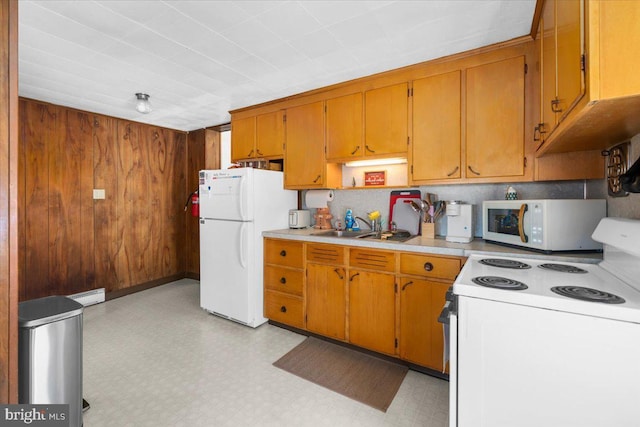 kitchen with a baseboard heating unit, white appliances, sink, and wood walls