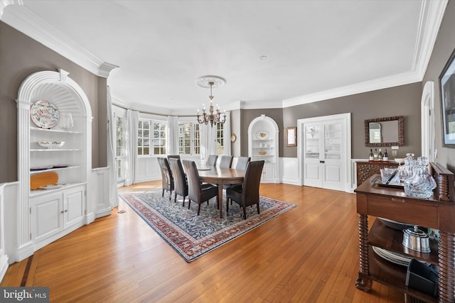 dining area featuring a notable chandelier, crown molding, built in features, and light wood-type flooring