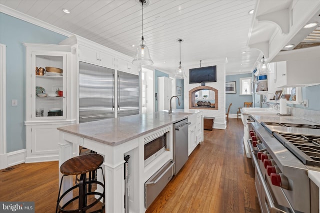 kitchen featuring sink, hanging light fixtures, built in appliances, an island with sink, and white cabinets