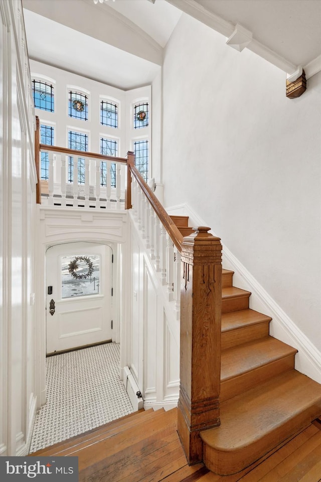 stairs with a baseboard radiator, hardwood / wood-style floors, and a high ceiling