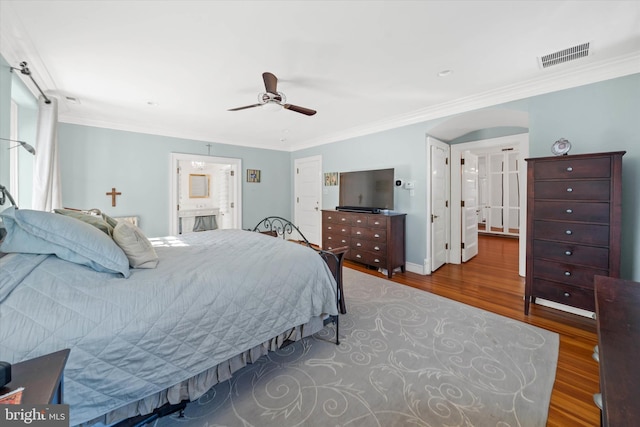 bedroom featuring crown molding, hardwood / wood-style flooring, ensuite bath, and ceiling fan