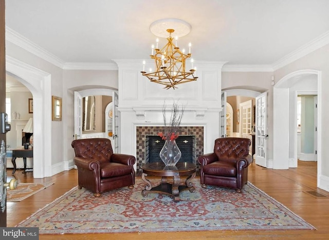 living area with crown molding, wood-type flooring, a fireplace, and a chandelier