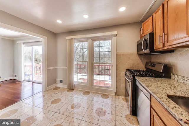 kitchen with ornamental molding, light stone countertops, a healthy amount of sunlight, and appliances with stainless steel finishes