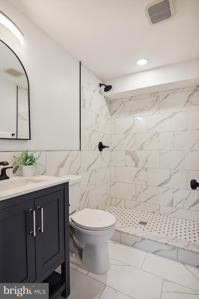 bathroom featuring vanity, a tile shower, tile walls, and toilet