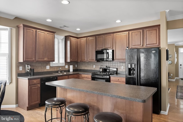 kitchen with light wood-type flooring, black appliances, a kitchen island, and tasteful backsplash