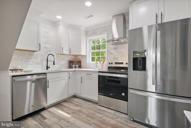 kitchen with wall chimney exhaust hood, sink, light hardwood / wood-style flooring, appliances with stainless steel finishes, and white cabinets