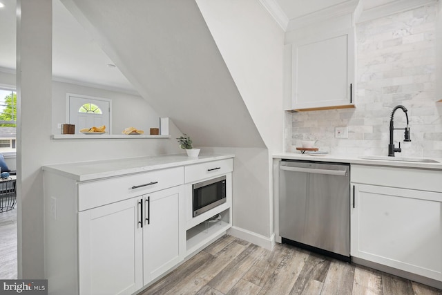 kitchen with appliances with stainless steel finishes, sink, white cabinets, backsplash, and light wood-type flooring