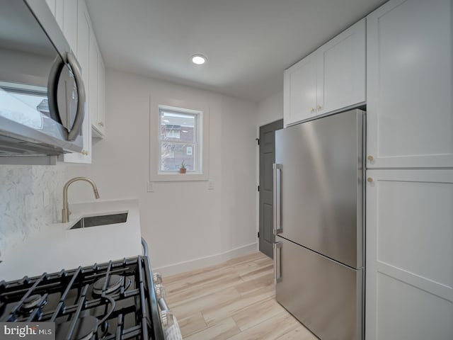 kitchen with appliances with stainless steel finishes, sink, white cabinets, backsplash, and light hardwood / wood-style flooring