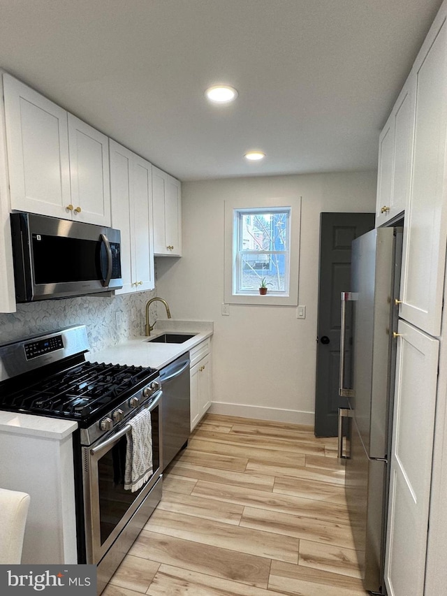 kitchen featuring sink, appliances with stainless steel finishes, tasteful backsplash, light hardwood / wood-style floors, and white cabinets