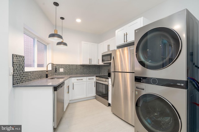 kitchen with hanging light fixtures, sink, white cabinets, stacked washer and clothes dryer, and stainless steel appliances