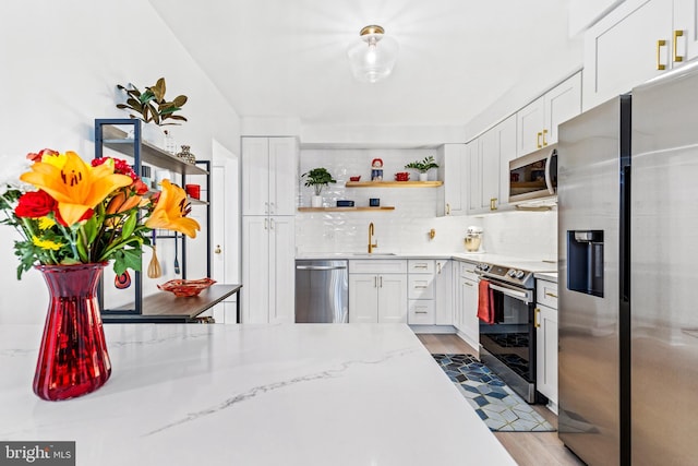 kitchen with sink, white cabinetry, tasteful backsplash, stainless steel appliances, and light stone countertops