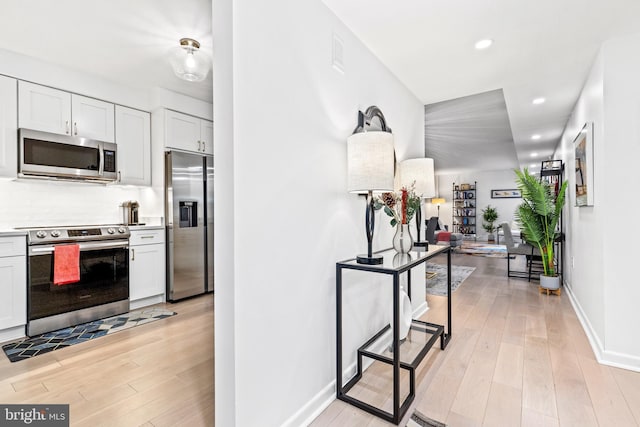 kitchen with stainless steel appliances, light hardwood / wood-style floors, decorative backsplash, and white cabinets