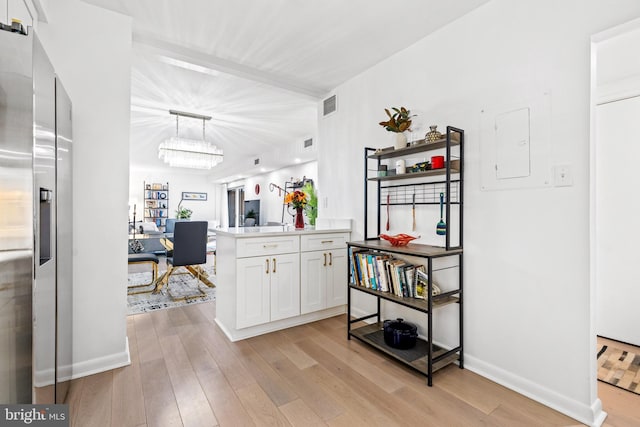 kitchen featuring pendant lighting, light hardwood / wood-style flooring, white cabinets, kitchen peninsula, and a chandelier