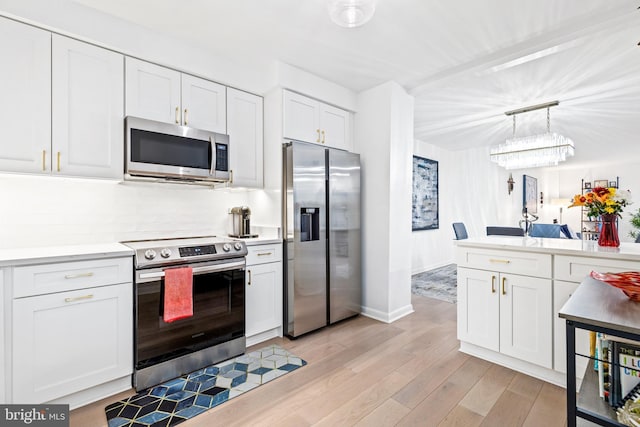 kitchen featuring pendant lighting, backsplash, stainless steel appliances, white cabinets, and light wood-type flooring