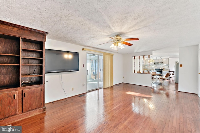 living room with light wood-type flooring, ceiling fan, and a textured ceiling