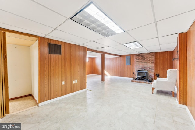 basement with a wood stove, wood walls, and a drop ceiling