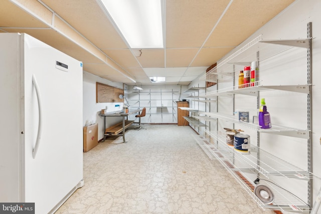 basement featuring white fridge and a drop ceiling