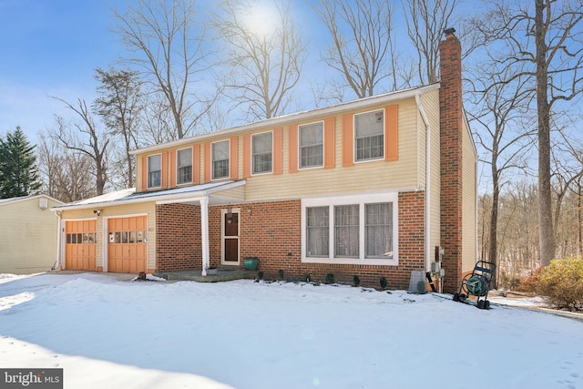 snow covered rear of property with a garage, brick siding, and a chimney