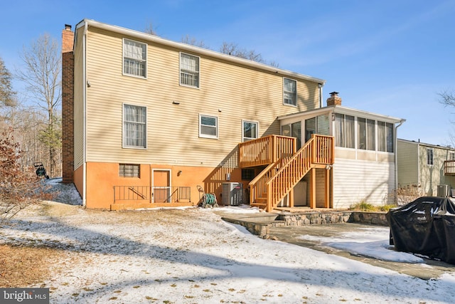 snow covered property with a deck, central AC unit, and a sunroom