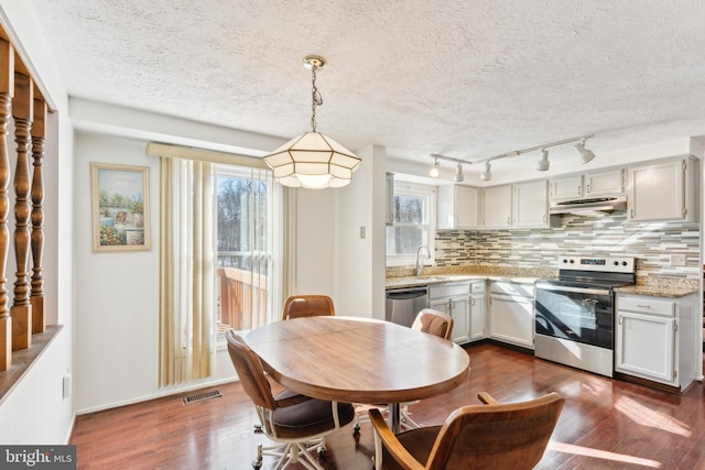 kitchen featuring light stone countertops, tasteful backsplash, decorative light fixtures, dark wood-type flooring, and stainless steel appliances