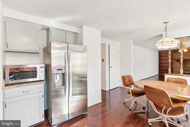 kitchen with light stone countertops, a textured ceiling, pendant lighting, dark wood-type flooring, and stainless steel fridge