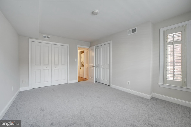 unfurnished bedroom featuring light carpet and two closets