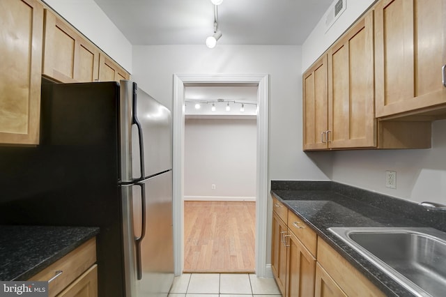 kitchen featuring dark stone counters, stainless steel fridge, sink, and light tile patterned floors