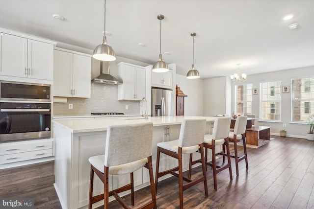 kitchen with appliances with stainless steel finishes, a breakfast bar area, a center island with sink, and wall chimney exhaust hood