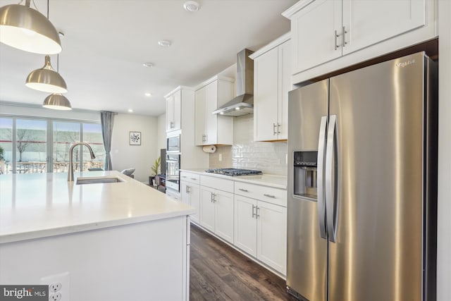 kitchen featuring white cabinetry, appliances with stainless steel finishes, pendant lighting, and wall chimney range hood