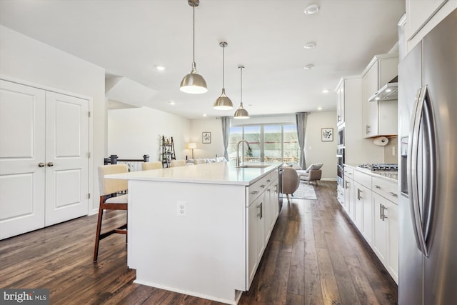 kitchen with appliances with stainless steel finishes, pendant lighting, white cabinetry, sink, and a center island with sink