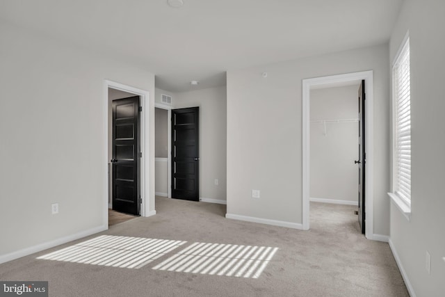 unfurnished bedroom featuring a closet, light colored carpet, a spacious closet, and multiple windows