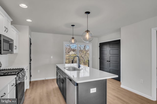 kitchen featuring appliances with stainless steel finishes, sink, decorative light fixtures, white cabinets, and a center island with sink