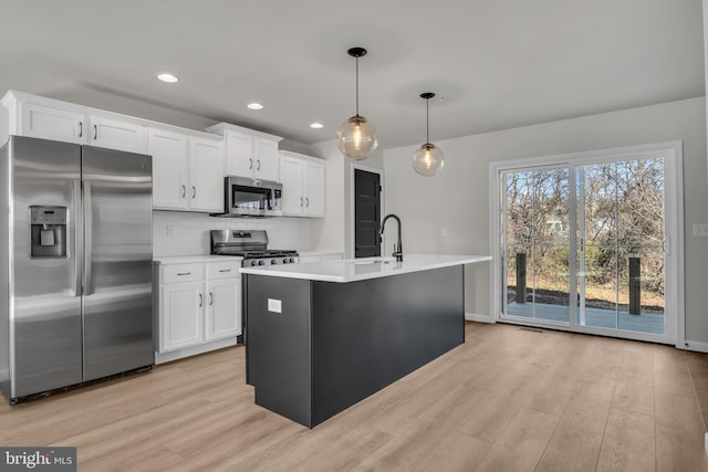 kitchen featuring decorative light fixtures, white cabinets, tasteful backsplash, an island with sink, and stainless steel appliances