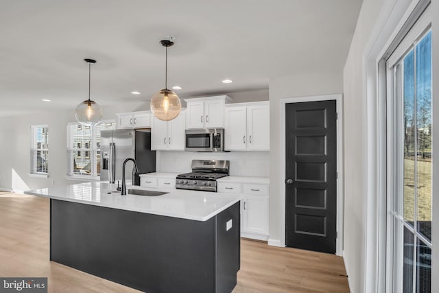 kitchen with pendant lighting, appliances with stainless steel finishes, white cabinetry, sink, and a kitchen island with sink