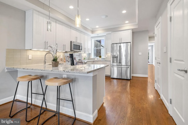 kitchen with white cabinets, appliances with stainless steel finishes, decorative backsplash, kitchen peninsula, and light stone counters